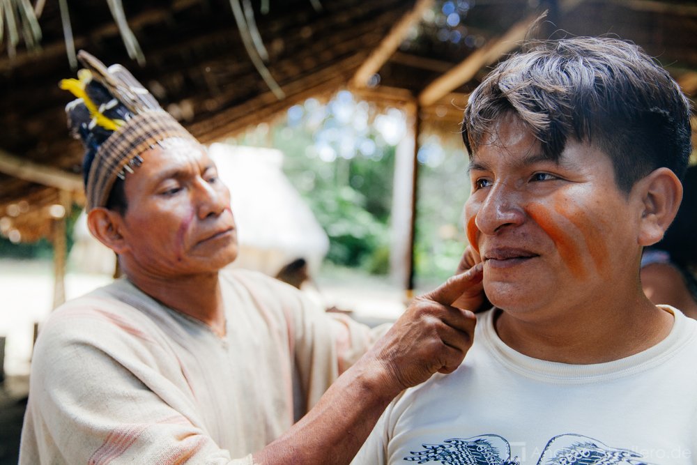 Artista indígena amazónico aplicando pintura facial tradicional a turista en experiencia cultural auténtica